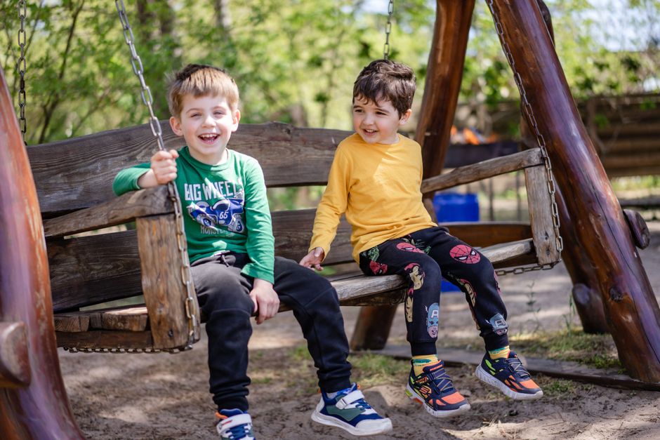 Two boys enjoying a playful moment on a wooden swing outdoors, sharing laughter.
