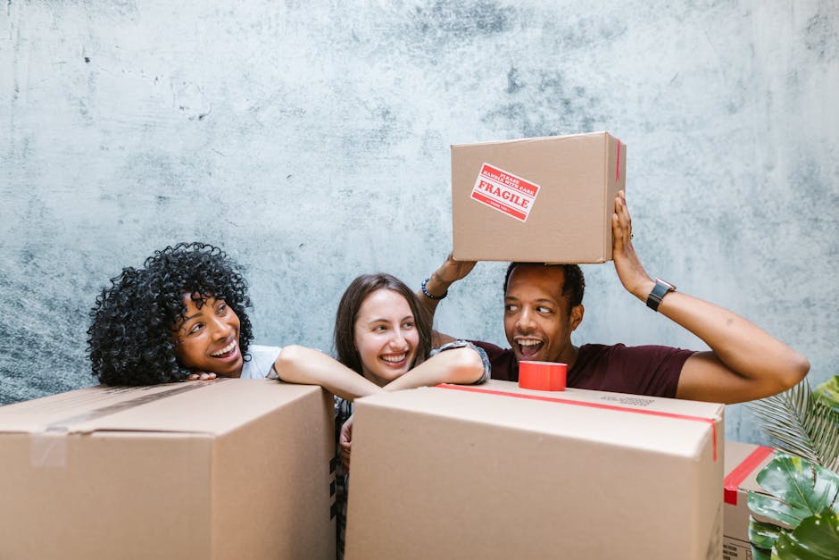 Diverse group of friends smiling while packing moving boxes. Relocation and new beginnings.