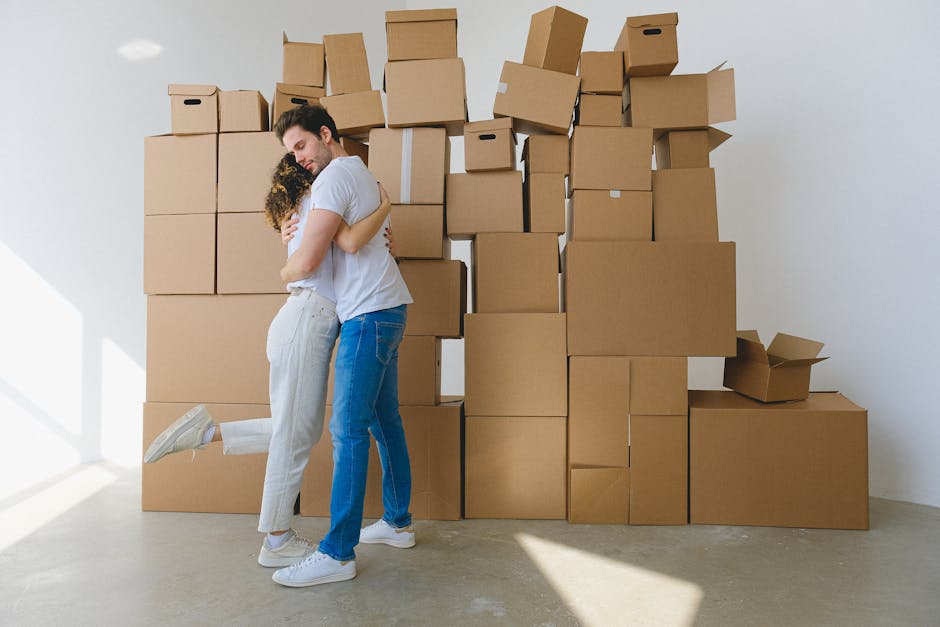 A couple embraces surrounded by stacked cardboard moving boxes, capturing a moment of transition indoors.