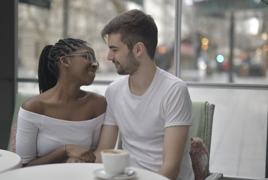 A loving multiracial couple shares a joyful moment over coffee, embracing affection and diversity indoors.