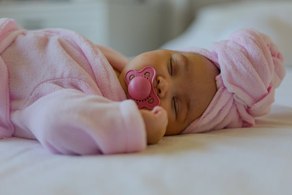 Peaceful newborn baby sleeping in pink attire with a pacifier indoors.