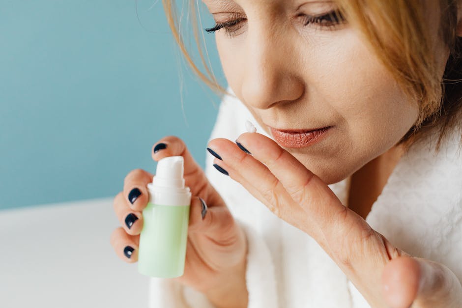Close-up of a woman in a bathrobe applying skincare cream, focusing on self-care and beauty routine.
