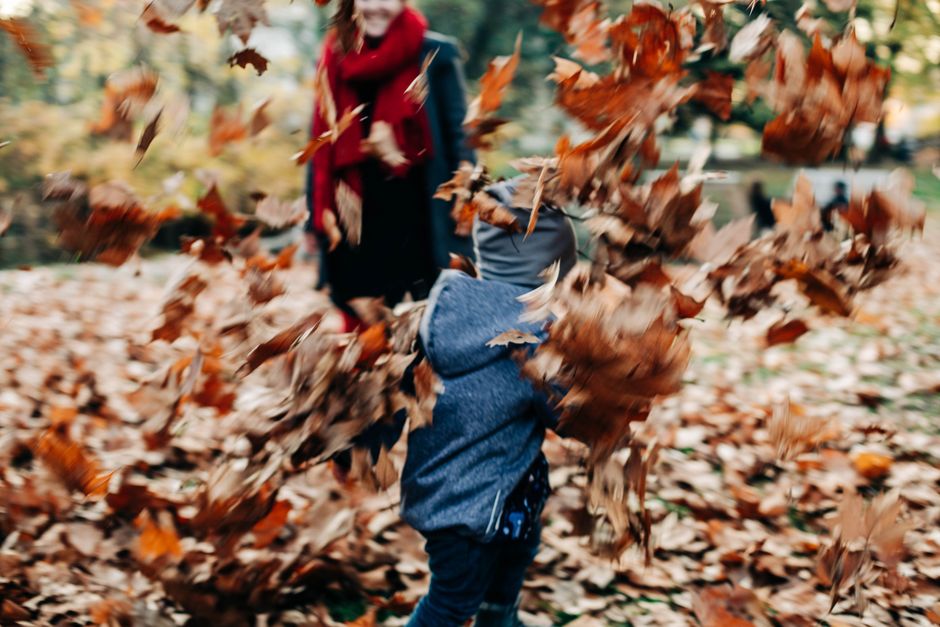 A joyful child running through colorful autumn leaves in a park setting.