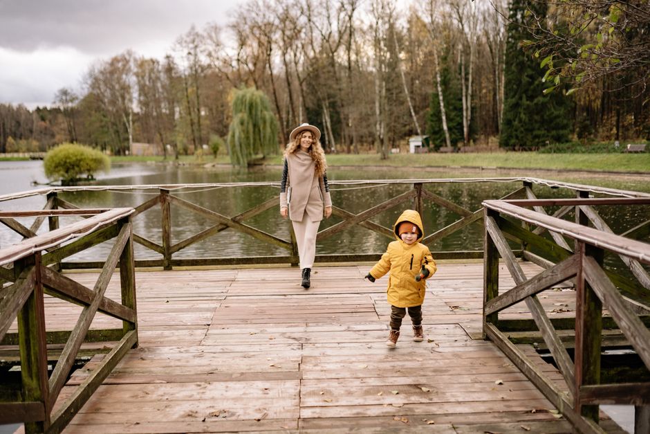 A mother and child enjoying a peaceful walk on a wooden dock during autumn in a scenic park.