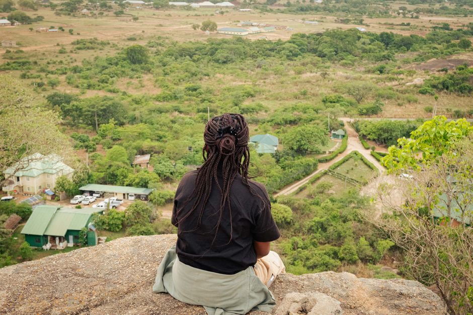 Woman with braids sits on cliff, overlooking the lush, rural landscape of Jos, Nigeria.