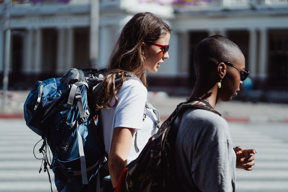 Two diverse women with backpacks exploring a city, enjoying their travel journey.