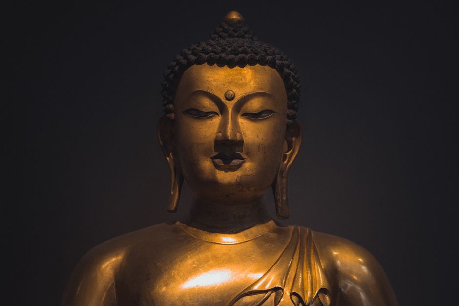 Close-up of a golden Buddha statue in a London museum, showcasing intricate details and serene expression.