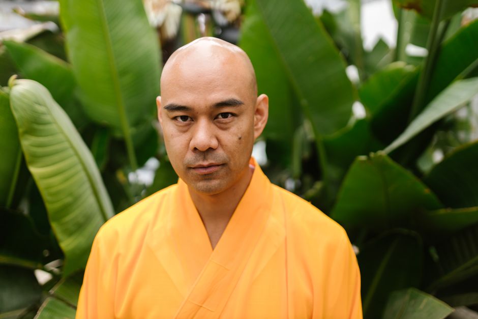Portrait of a Buddhist monk in orange robe surrounded by green leaves symbolizing serenity.