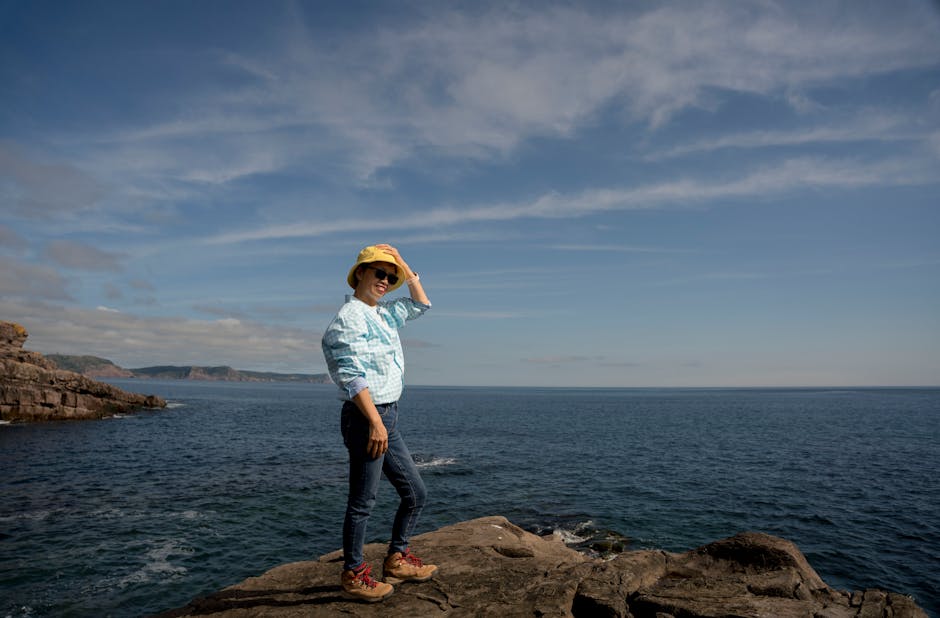 An Asian woman smiling on a coastal cliff, enjoying a sunny summer day by the ocean.