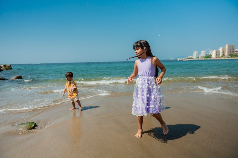 Two kids enjoying a sunny day on a sandy beach with clear blue skies and gentle waves.