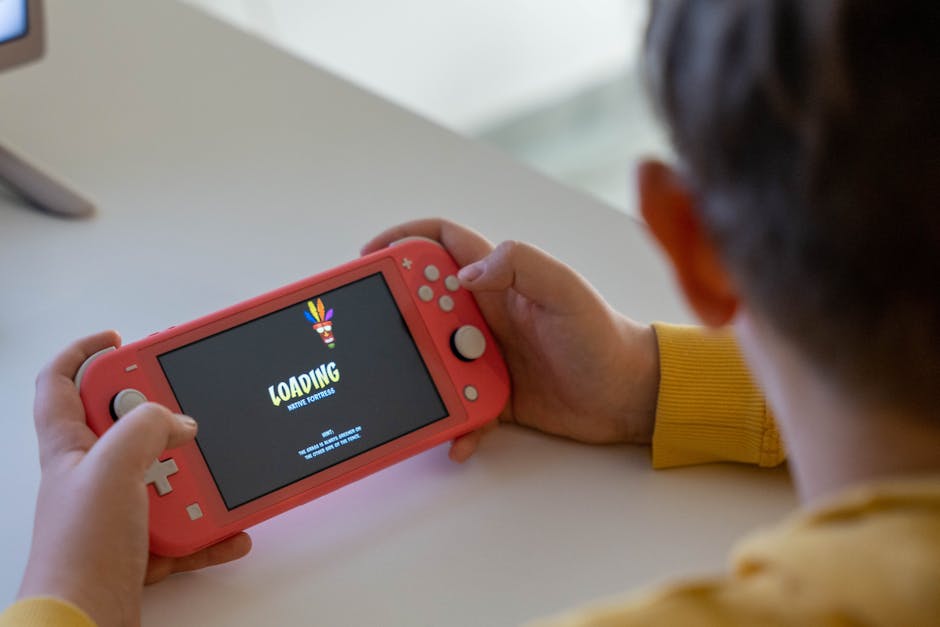 Child holding a pink handheld game console while a digital game loads on the screen.