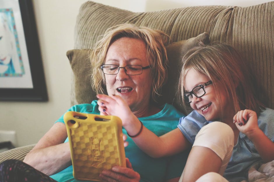 A joyful grandmother and grandchild bonding over a tablet on a cozy sofa indoors.