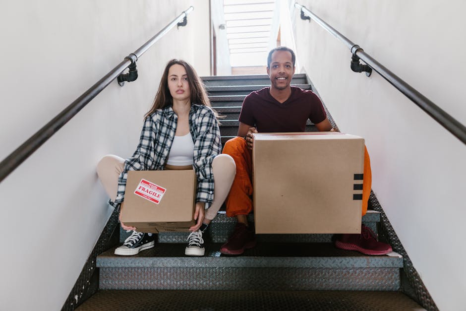 Interracial couple sitting on stairs with cardboard boxes, ready for moving.