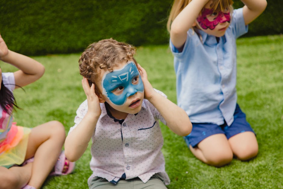 Children with face paint enjoy an outdoor birthday party on a lawn, celebrating with playful innocence.