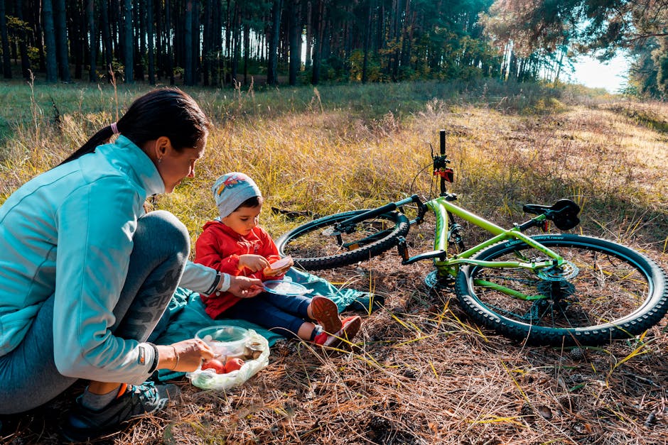 Mother and son having a picnic in the forest with a bicycle nearby, enjoying a sunny day outdoors.
