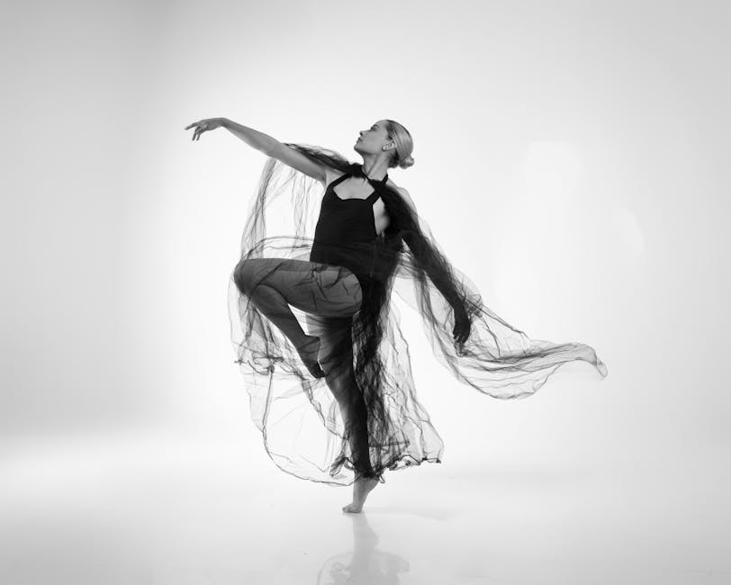 Black and white portrait of a graceful dancer in flowing dress captured mid-pose in studio.