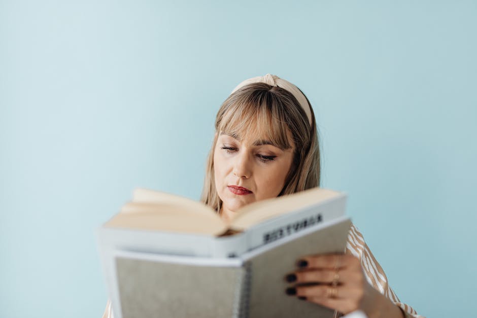 Caucasian woman with headband intently reading a book against a blue background.