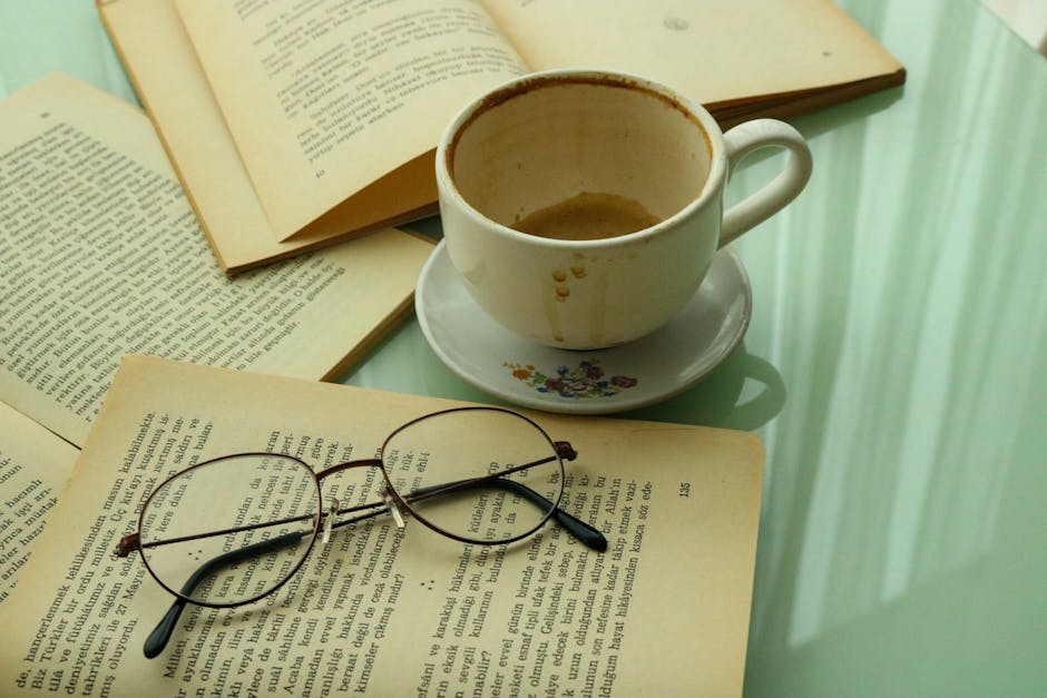 Vintage-style reading setup with books, ceramic cup, and eyeglasses.