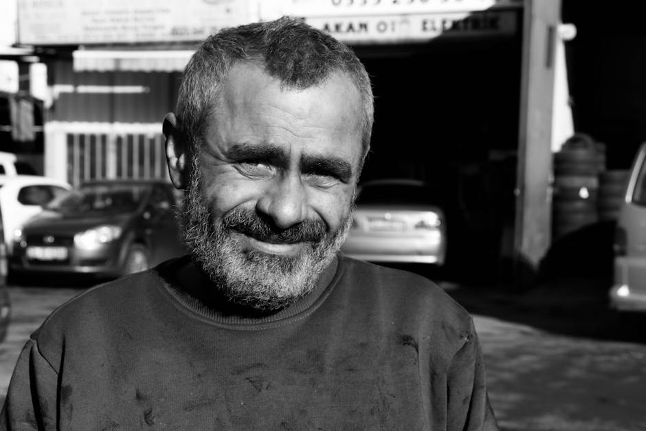 A compelling black and white portrait of a smiling man outdoors in a casual setting.